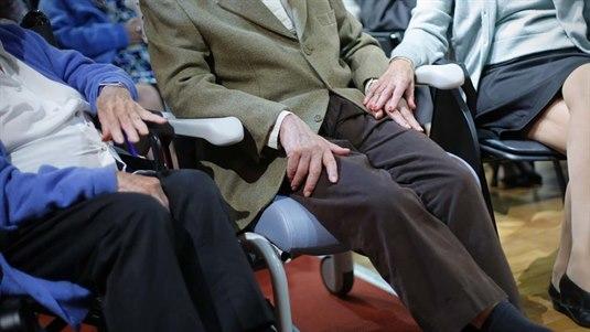 Pent kledd eldre par som sitter på et legekontor. Hun holder over hans hånd.