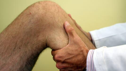 Behandler som undersøker kne til en mannlig pasient