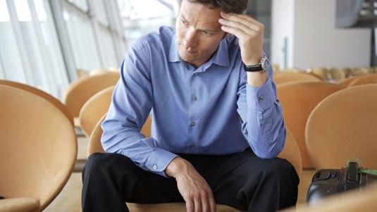 Man sitter på en stol i et lokale og holder ene hånden mot pannen