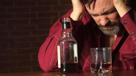 Mann sitter i en bar med et halvt glass whisky og en flaske som er nesten tom