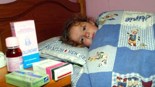 medisin barn Et barn som ligger i sengen og som har flere typer medisin på nattbordet