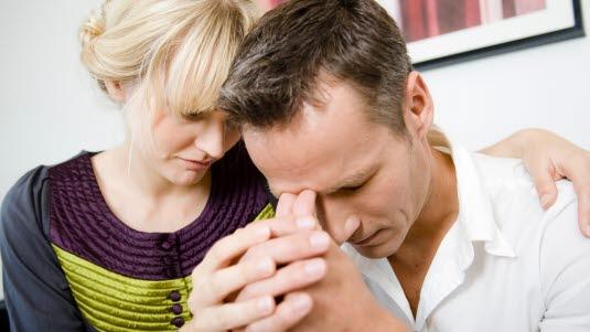 Å dele en krise Et par sitter sammen i sofaen hvor hun holder rundt mannen som lener pannen mot tomlene