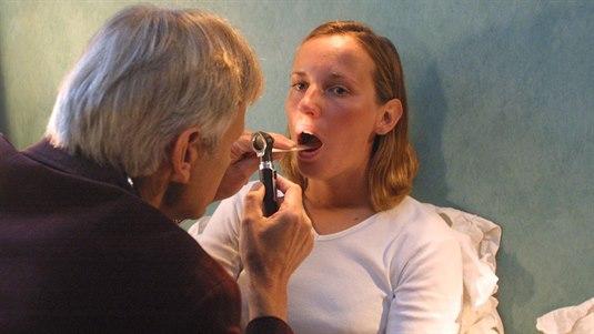 Munn.jpg Lege undersøker munnen til en pasient med et otoskop og en munnpinne