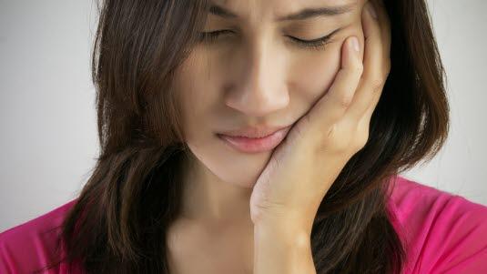 Ansiktssmerter Illustrasjonsfoto av ung kvinne som holder en hånd over kjeven og ser plaget ut