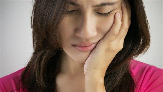 Ansiktssmerter Illustrasjonsfoto av ung kvinne som holder en hånd over kjeven og ser plaget ut