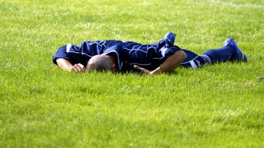 Idrettsbrokk En fotballspiller ligger med kroppen ned mot gresset