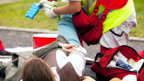 Idrettsskade Liggende pasient utendørs får foten undersøkt av Ambulansearbeider for blødning