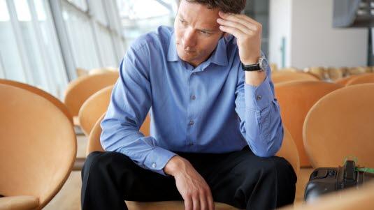 hodepine Man sitter på en stol i et lokale og holder ene hånden mot pannen