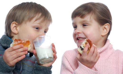 Spiser To småbarn som sitter og spiser sjokoladeboller med et glass melk