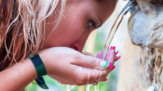 Tørst jente/dame En kvinne holder hendene under en rennende vannfontene for å drikke. Mens vannet renner ned i hendene hennes og hun tar en slurk.