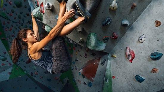 Buldring Illustrasjonsfoto: Ung kvinne med langt mørkt hår klatrer på innendørs klatrevegg.